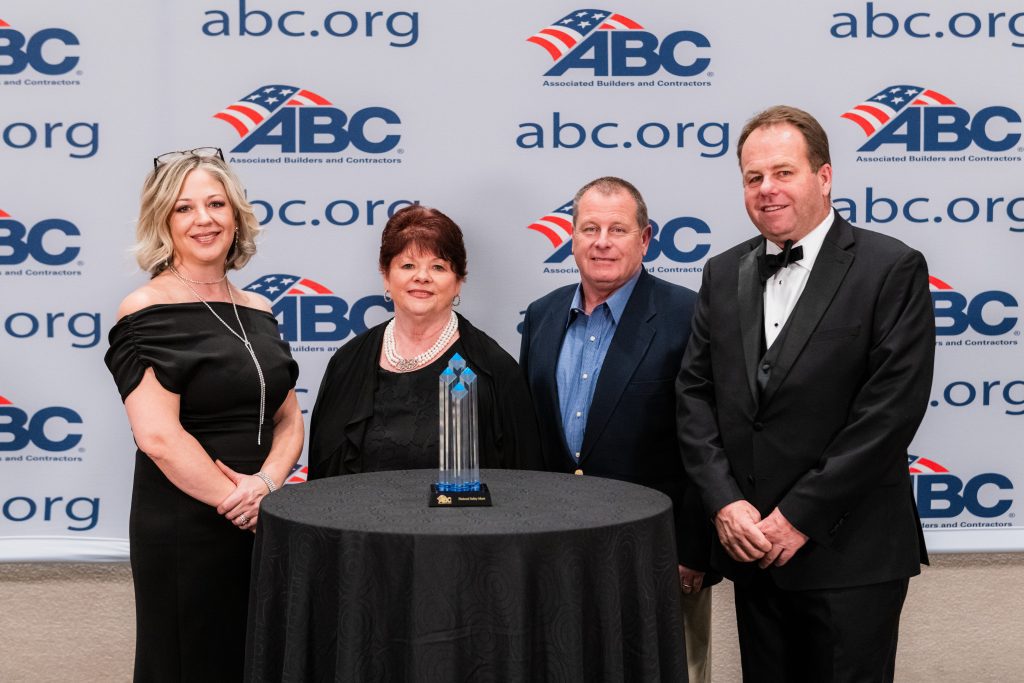 Four people stand around a table with an award on it, in front of an ABC backdrop.